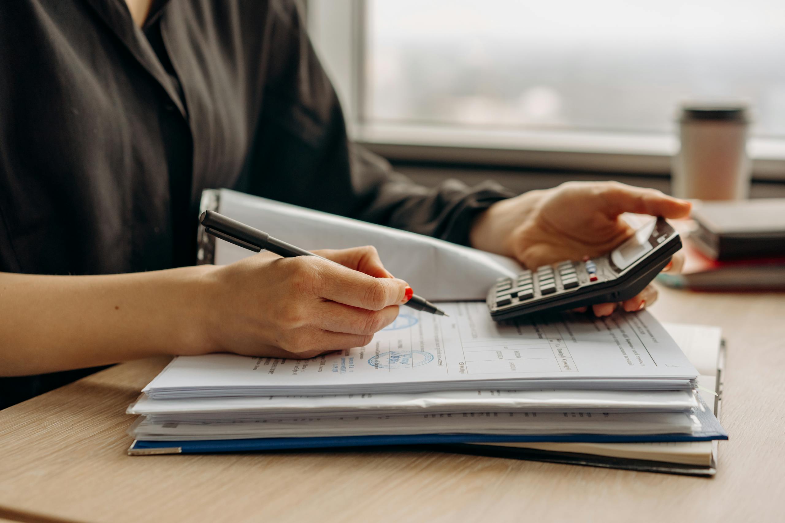 Zesty for Accountants 6 Close-up of person using a calculator with financial documents in an office.