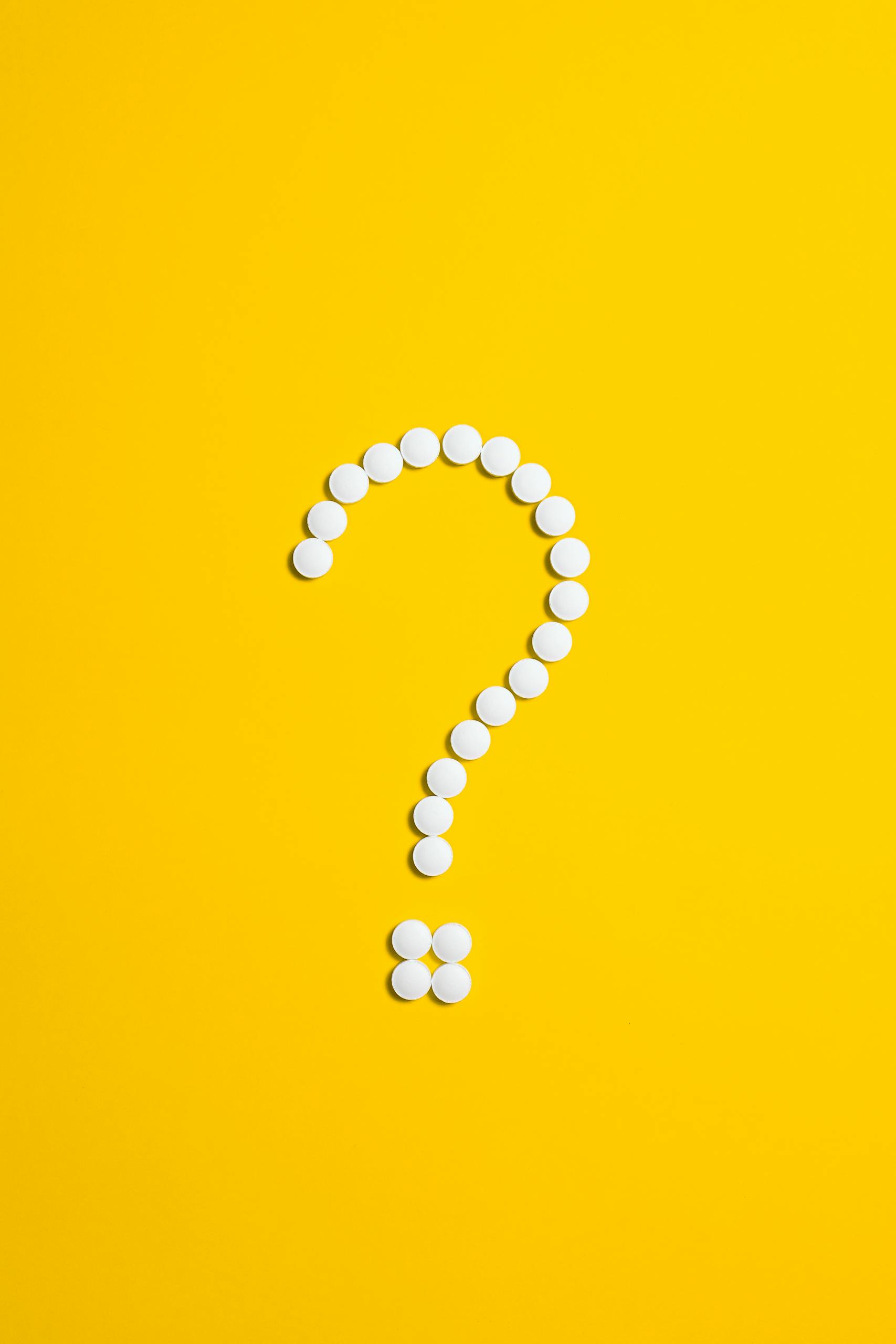 Zesty for Early Childhood Education | ECE Admin 5 White pills arranged in a question mark shape on a bright yellow background, symbolizing medical queries.